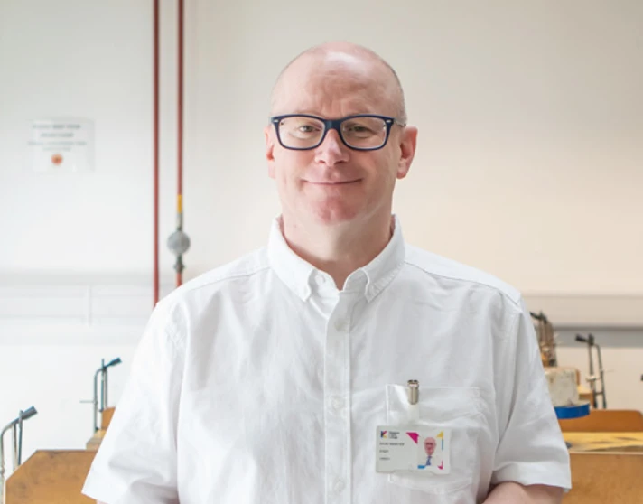 Lecturer David Webster stands in a jewellery workshop at Glasgow Kelvin College, smiling and holding a jeweller’s saw, with tools and benches in the background. Lecturer David Webster stands in a jewellery workshop at Glasgow Kelvin College, smiling and holding a jeweller’s saw, with tools and benches in the background.